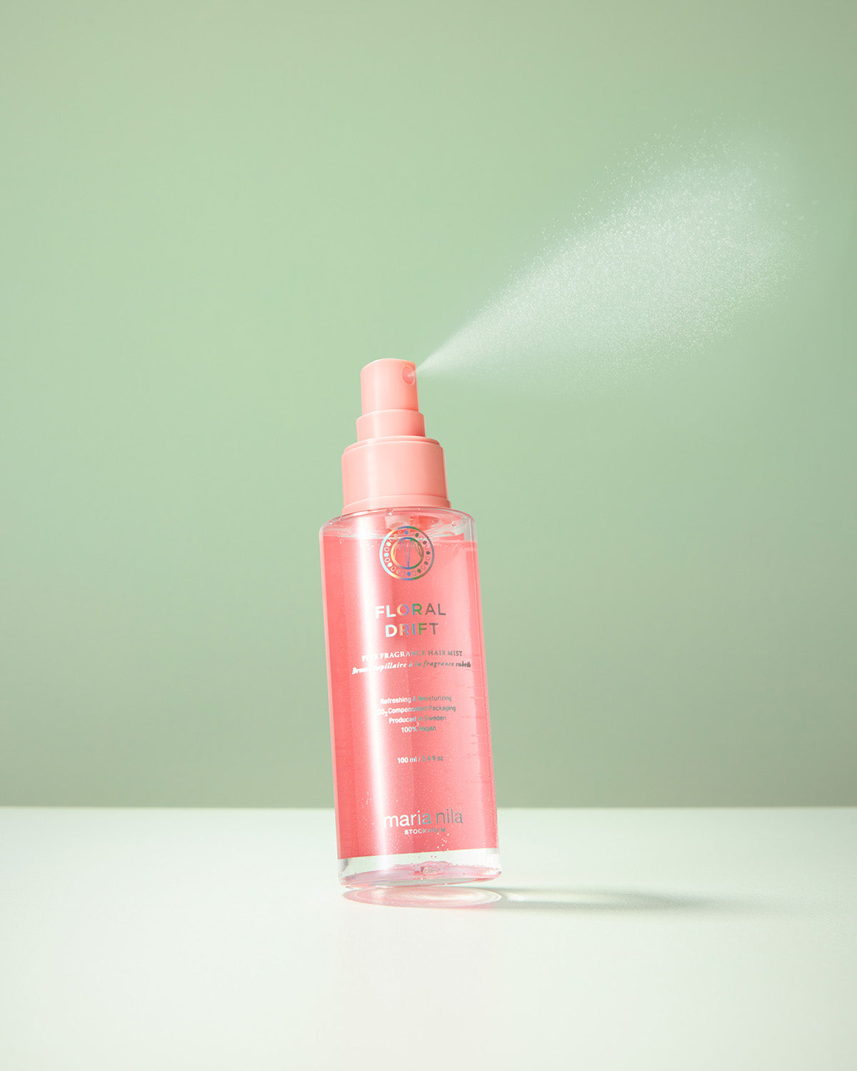 Pink spray bottle of Maria Nila Floral Drift hair mist on a light green background